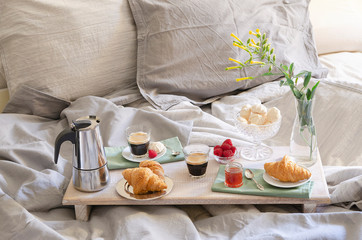 Romantic Breakfast  or brunch for two in bed. Coffee maker  and coffee glasses, croissants, jam, berries, meringue and flowers on wood tray. Romantic good morning scenery