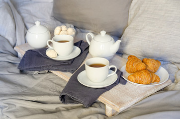 Breakfast In Bed : teapot, two cup of tea, croissants and meringue on wooden tray. Good morning scenery background. Scandinavian style.
