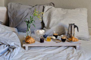 Luxury breakfast in the bed in hotel bedroom. Coffee maker  and coffee glasses, croissants, jam, raspberry meringue and flowers on wood tray .Good morning surprise concept.