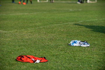 Colourful bibs left on a football pitch, ready for the next training session to come while footballers are drilling on the pitch with a coach and a clear sky in summer time.