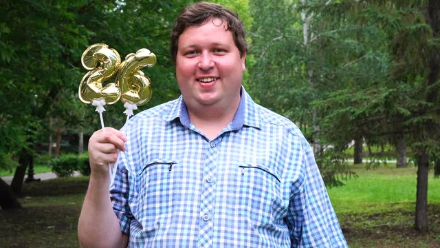 Big man holding golden balloons making the 26 number outdoor. 26th anniversary celebration party