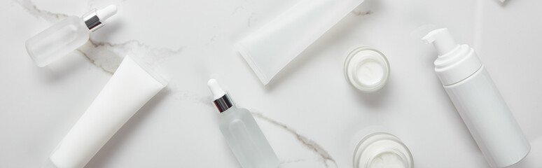 panoramic shot of cosmetic glass bottles, jars with cream, moisturizer tubes and dispenser on white...