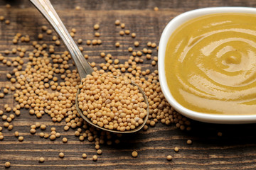 Mustard. mustard sauce in a bowl and dry mustard seeds on a brown wooden table. close-up