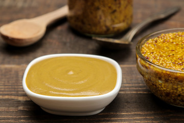 Mustard french and mustard sauce in a bowl on a brown wooden table. close-up.