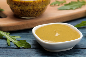 Mustard sauce and mustard in a bowl on a blue wooden table. close-up.