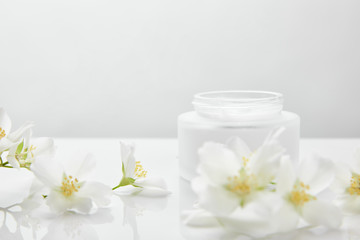 Fototapeta na wymiar jasmine flowers on white surface near jar with cream