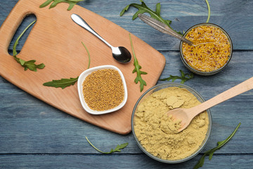 french mustard in a bowl and dry mustard seeds and powders on a blue wooden table. top view
