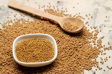 dry mustard seeds in a bowl on a light concrete table. cooking mustard sauce close-up.