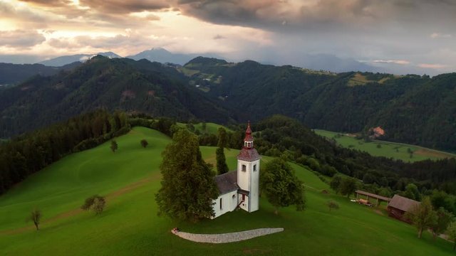 Skofja Loka, Slovenia - 4K aerial footage of flying around of the small Sveti Tomaz (Saint Thomas) church at sunset at summer time with beautiful golden clouds