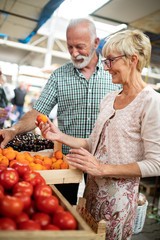 Senior couple buying fresh vegetables and fruits at the local market