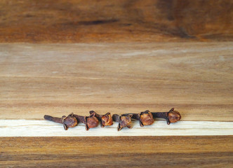 Cloves sticks in a soft focus on wooden table in rustic style, closeup.