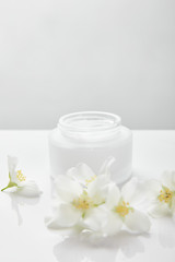 Fototapeta na wymiar jasmine flowers on white surface near jar with cream