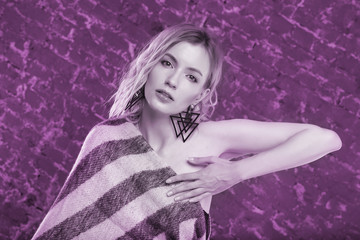 Portrait of a young sexy female fashion model in wool blanket on brick wall background. Photo tinted in purple.