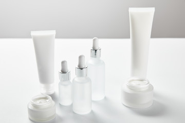 cream tubes, cosmetic glass bottles and open jars with cream on white