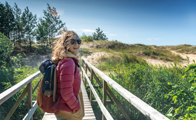 Young happy beautiful girl walks along the cold shore of the Baltic Sea in windy sunny weather, traveling to the Scandinavian countries - obrazy, fototapety, plakaty