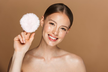 Beautiful smiling young amazing woman posing isolated over brown chocolate background wall holding powder puff.