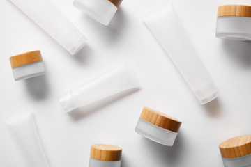 scattered jars and cream tubes for cosmetic products on white