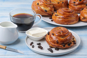 Delicious buns with raisins and butter and coffee with milk on a light blue wooden table. fresh bakery. breakfast. bread.