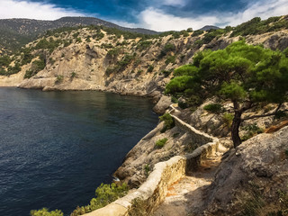 Fototapeta na wymiar view of secluded sea bay in the summer from a mountain path surrounded by mountain cliffs with lush pine and ancient mountain path along the coast, idyllic seascape, Golitsina trail in the Crimea