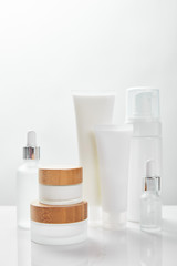 Fototapeta na wymiar white surface with glass bottles, cream in tubes, jars and cosmetic dispenser