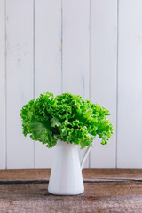 Fresh lettuce green leaves in the white mug on rustic background