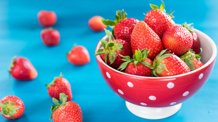 colorful ripe strawberries in a bright bowl on a blue background