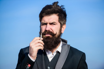 Bearded hipster smoking cigarette blue sky background. Guy with cigarette enjoy nicotine influence....