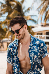 Handsome mature male model enjoying a sunny day on the beautiful island of Boracay. Walking with open blue shirt between palm trees on famous white beach.