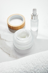 Fototapeta na wymiar opened jar with cosmetic cream and glass bottle near towel on white surface