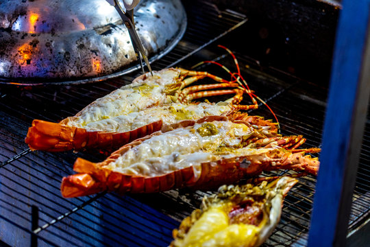 Cooking lobsters on the grill on the street food market in Bangkok in Thailand. He using chrome tongs. Closeup horizontal photo.