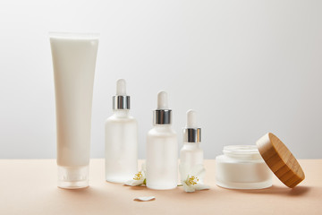 cream tube, cosmetic glass bottles, open jar with cream and few jasmine flowers on beige - obrazy, fototapety, plakaty