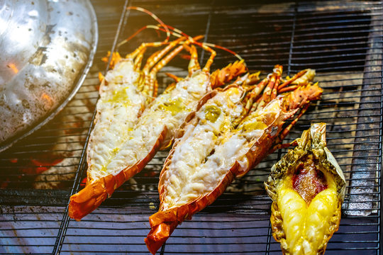 Cooking lobsters on the grill on the street food market in Bangkok in Thailand. He using chrome tongs. Closeup horizontal photo.