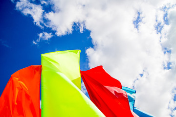 Colorful red and yellow flags waving on bright blue sky background with white fluffy clouds