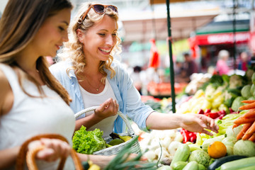 Young happy women shopping vegetables and fruits on the market