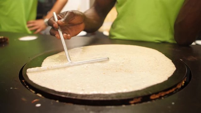Cook spreading golden crepe batter across a griddle.
