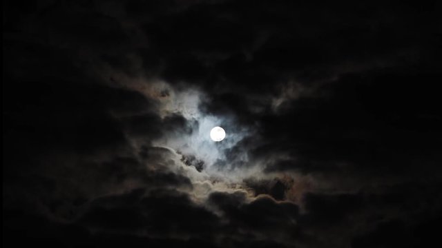 Wide time lapse of slowly rising full moon with halo behind clouds, copy