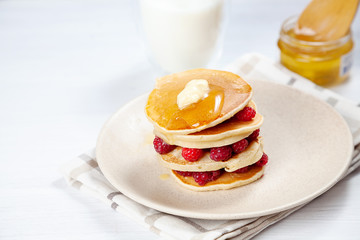 Closeup on stack of fresh, homemade pancake stack with raspberry, melting butter and pouring honey or marple syrup. american pancake on white background with morning light. Breakfast. selective focus.