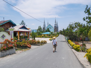 Woman with traditional hat walking in the street of Ngurbloat, a tiny colorful flowery village with a huge christian gotic style church in Kei Islands, Moluccas Indonesia.