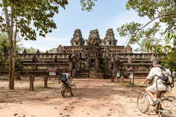 Obraz premium Tourist couple cycling around Angkor temple, Cambodia. Ta Keo building ruins in the jungle. Eco friendly tourism traveling, toned image.