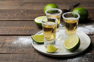 Gold tequila in a glass with salt and lime on a brown wooden table. alcoholic beverages.