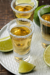 Gold tequila in a glass with salt and lime on a brown wooden table. alcoholic beverages.