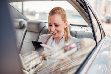 Elegant businesswoman texting on smart phone on backseat of the car.
