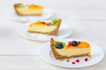 A few slices of cheesecake with fruit on white plates.