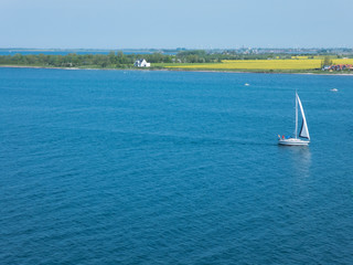 ein einsames Segelboot fährt durch den Fehmarn Sund;  im Hintergrund die Insel Fehmarn
