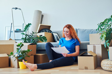 Young woman sitting on floor in new apartment with smartphone and documents