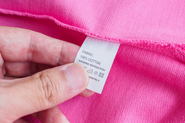 Woman reading on laundry care washing instructions clothes label on pink cotton shirt