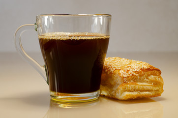 Coffee in a transparent cup. Puff bun with sesame on a glass surface. Bubbles in coffee