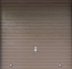 Full frame background of a light brown garage door with a metal handle and air vents.
