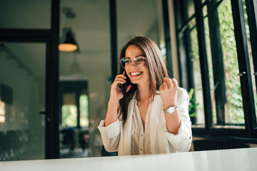 Smiling millennial entrepreneur talking on mobile phone at modern office.