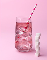 Glass of pink soda water with ice and striped straw with sugar cubes at pink background.